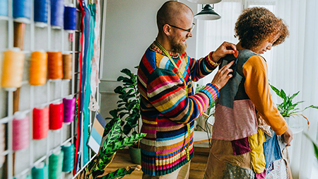 Smiling man measuring woman for an outfit he is making with recycled fabric